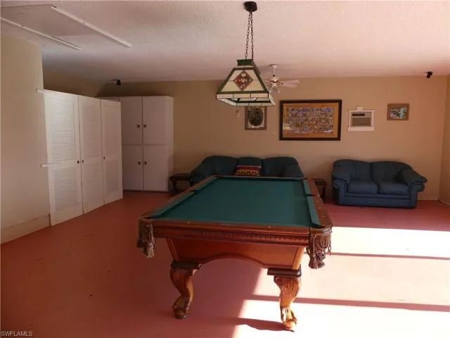 Recreation room featuring a textured ceiling, concrete flooring, a ceiling fan, billiards, and a wall mounted air conditioner in the clubhouse