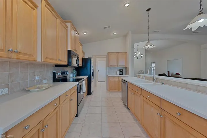 Kitchen with lofted ceiling, light brown cabinetry, sink, pendant lighting, and stainless steel appliances