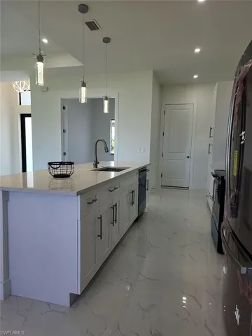 Kitchen featuring light tile patterned flooring, white cabinets, an island with sink, light stone countertops, and sink