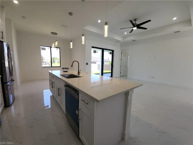 Kitchen with black refrigerator, an island with sink, sink, a raised ceiling, and light tile patterned floors