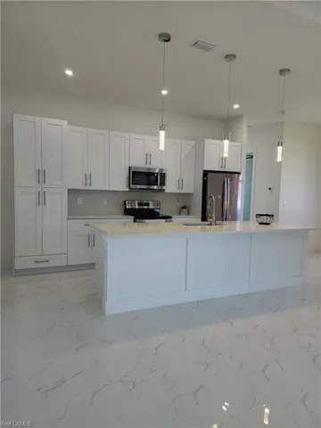Kitchen with light tile patterned flooring, decorative light fixtures, white cabinetry, a center island with sink, and appliances with stainless steel finishes