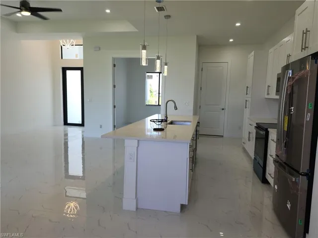 Kitchen featuring light tile patterned flooring, white cabinetry, stainless steel refrigerator, a kitchen island with sink, and ceiling fan