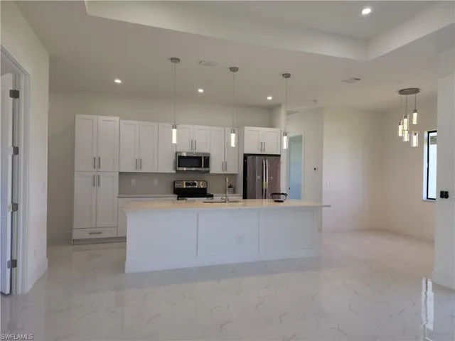 Kitchen with light tile patterned flooring, stainless steel appliances, white cabinets, sink, and a center island with sink