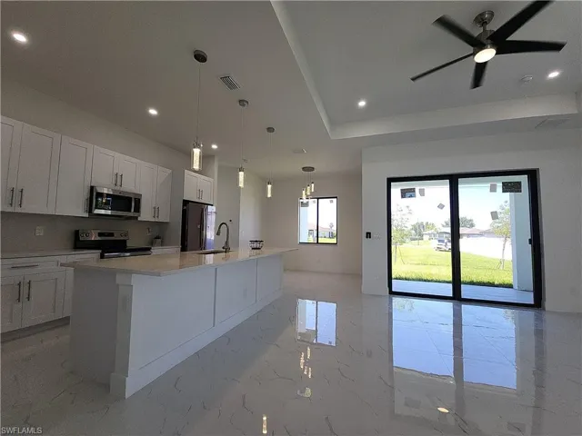 Kitchen featuring white cabinets, stainless steel appliances, light tile patterned floors, an island with sink, and ceiling fan