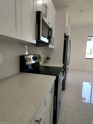 Kitchen with tasteful backsplash, stainless steel appliances, white cabinets, light stone counters, and light tile patterned flooring