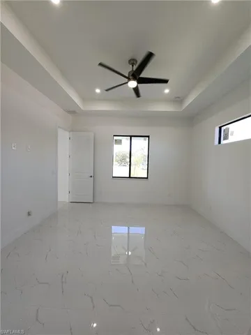 Tiled empty room featuring a tray ceiling and ceiling fan