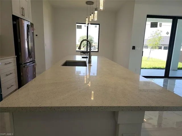 Kitchen featuring stainless steel fridge, plenty of natural light, light stone counters, and an island with sink