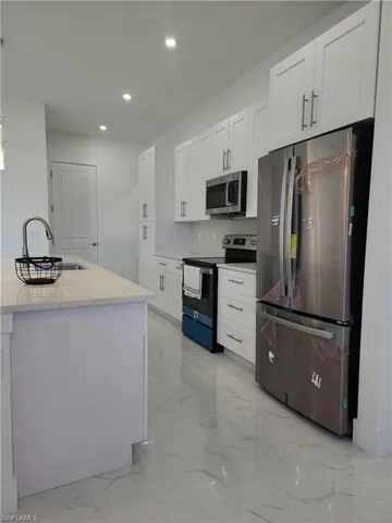Kitchen with white cabinets, stainless steel appliances, light stone counters, and sink