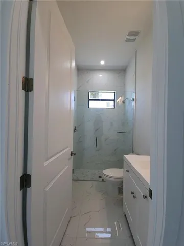 Bathroom with tiled shower, tile patterned floors, vanity, and toilet
