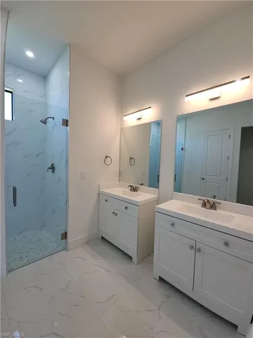 Bathroom with tile patterned floors, double sink vanity, and a tile shower