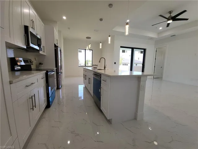 Kitchen with appliances with stainless steel finishes, light tile patterned flooring, white cabinetry, and a center island with sink