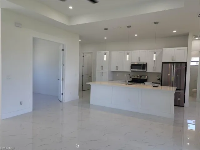 Kitchen with appliances with stainless steel finishes, hanging light fixtures, light tile patterned floors, and an island with sink
