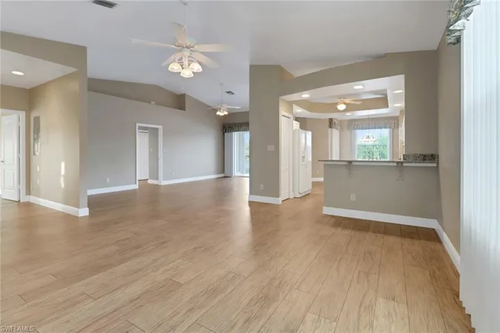 living room with light wood-style flooring, baseboards, a raised ceiling, and ceiling fan
