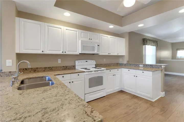 Kitchen with white cabinetry, granite counter tops, light wood-type flooring, and white appliances