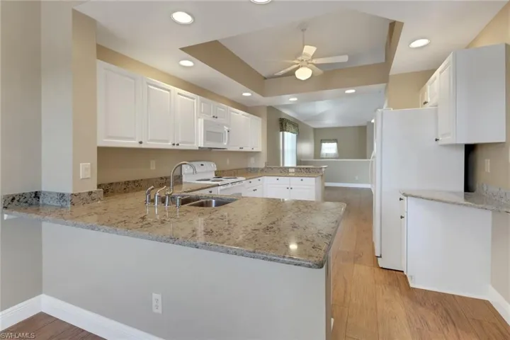 Kitchen with white appliances, light wood finished floors, a ceiling fan, and a peninsula