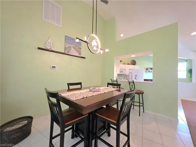 Dining space with light tile patterned floors, a chandelier, and vaulted ceiling