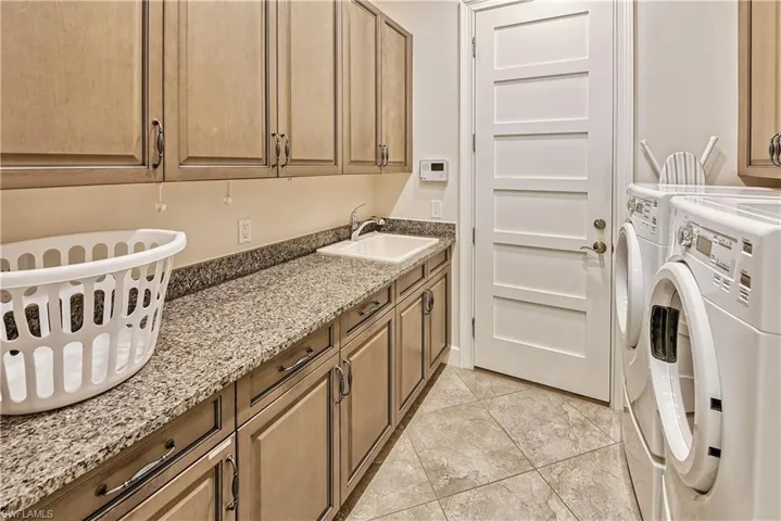 Clothes washing area featuring washing machine and dryer, sink, and cabinets