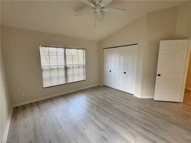 Room featuring vaulted ceilings, wood-finish flooring, a window with horizontal blinds, a ceiling fan, and a bi-fold closet