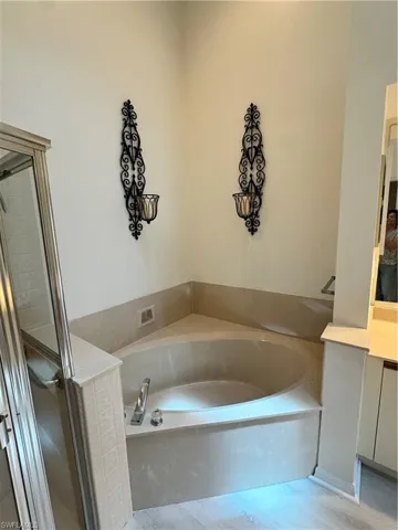 Corner soaking tub with a tiled surround, chrome fixtures, and adjacent glass-enclosed shower