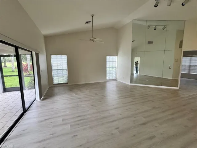 Spacious interior featuring wood-finish flooring, a vaulted ceiling, and an expansive mirrored wall