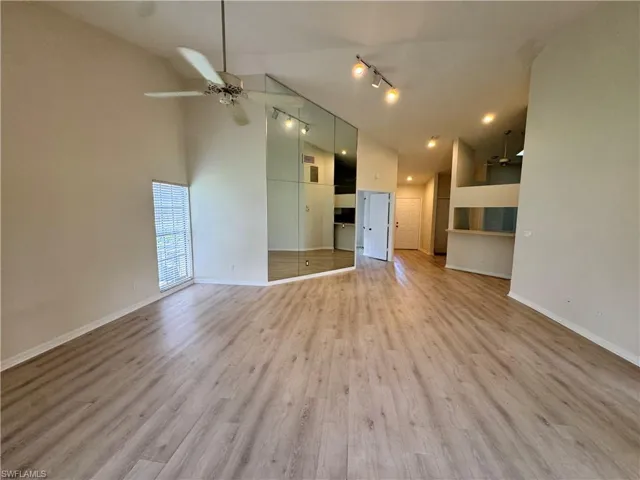 Spacious room featuring wood-finish flooring, a vaulted ceiling with a ceiling fan, and track lighting
