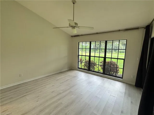 Vaulted ceiling room featuring light wood-finish flooring, a contemporary ceiling fan, and a large multi-pane window overlooking a green landscape