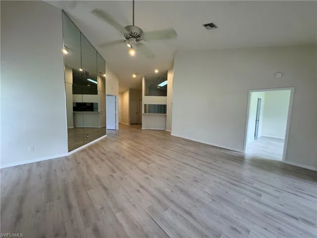 Spacious room featuring vaulted ceilings, wood-finish flooring, a contemporary ceiling fan with integrated lighting, and a mirrored accent wall