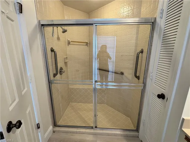 Shower enclosure with sliding glass doors, textured beige wall tile, floor tile in a diagonal pattern, built-in shower bench, and two grab bars