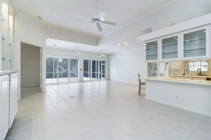 Unfurnished living room with crown molding, ceiling fan, a raised ceiling, and light tile patterned floors