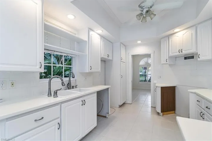 Kitchen with white cabinetry, light tile patterned flooring, ceiling fan, decorative backsplash, and sink