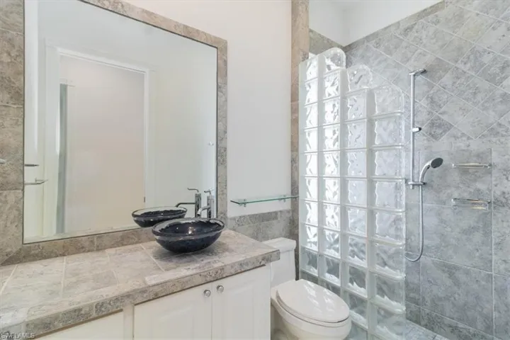Bathroom featuring vanity, tiled shower, toilet, and tile walls