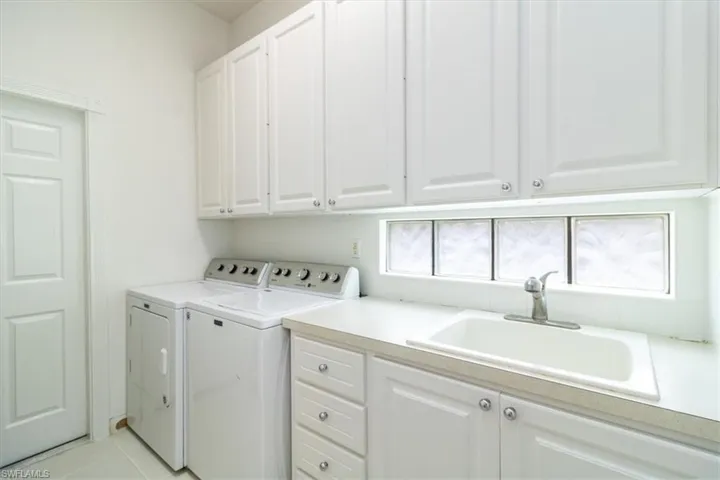 Clothes washing area featuring light tile patterned flooring, washer and clothes dryer, sink, and cabinets