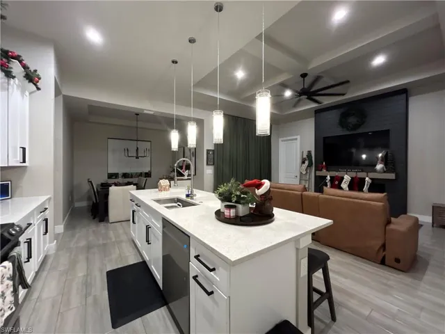 Kitchen featuring open floor plan, white cabinetry, light stone countertops, coffered ceiling, and a kitchen breakfast bar