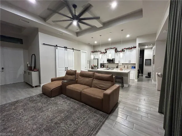 Living area with a barn door, a raised ceiling, wood tiled floors, a ceiling fan, and recessed lighting