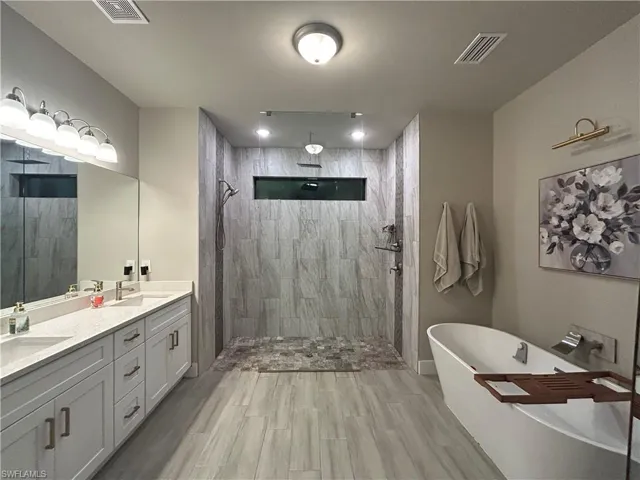 Bathroom with double vanity, walk in shower, a soaking tub, and wood looking finish floors