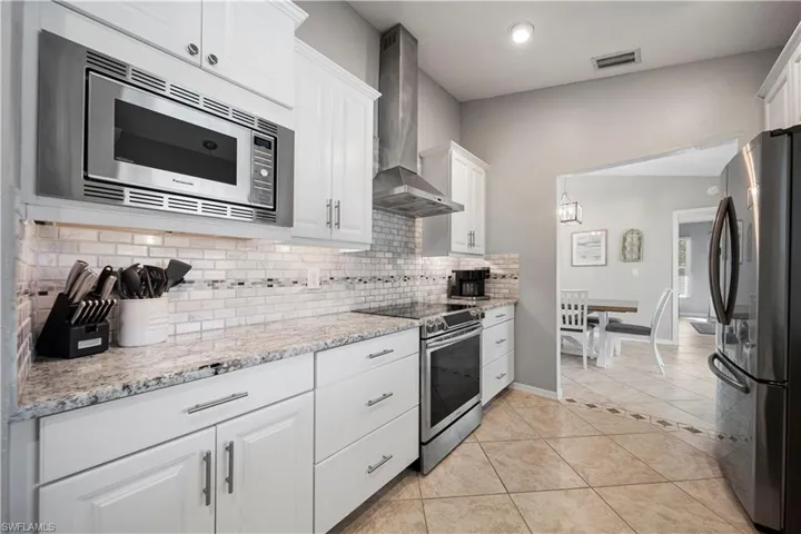 Kitchen with stainless steel appliances, tasteful backsplash, white cabinets, light tile patterned flooring, and wall chimney exhaust hood