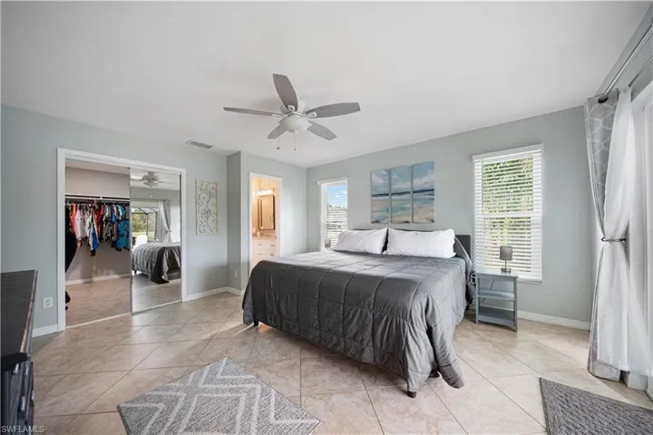 Bedroom featuring light tile patterned flooring, ceiling fan, ensuite bath, and a walk in closet