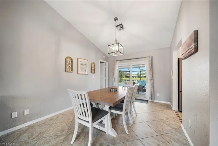 Dining room with lofted ceiling, light tile patterned floors, and a notable chandelier