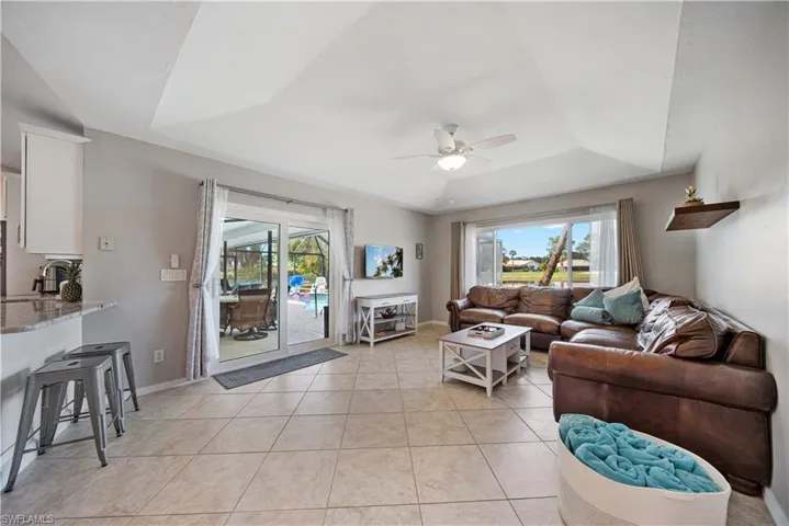 Living room with light tile patterned floors, a tray ceiling, plenty of natural light, and ceiling fan
