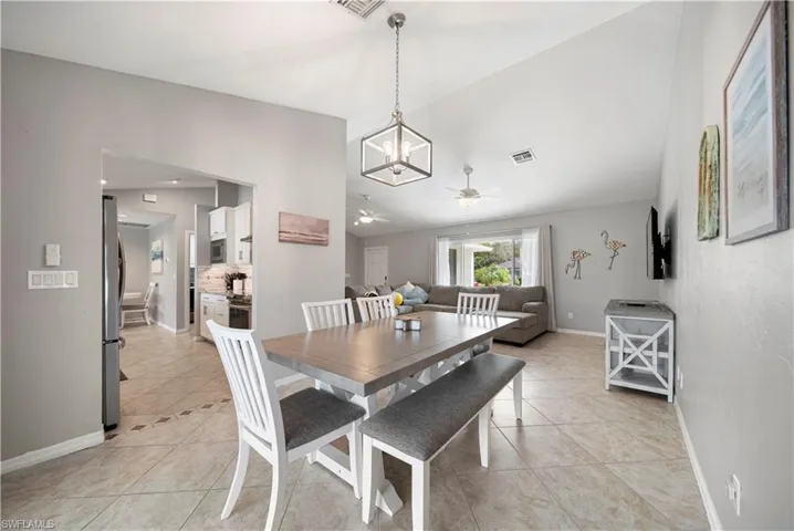 Dining area with lofted ceiling, light tile patterned floors, and ceiling fan with notable chandelier