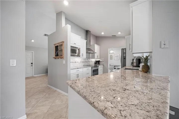 Kitchen featuring white cabinets, light stone countertops, kitchen peninsula, and wall chimney exhaust hood