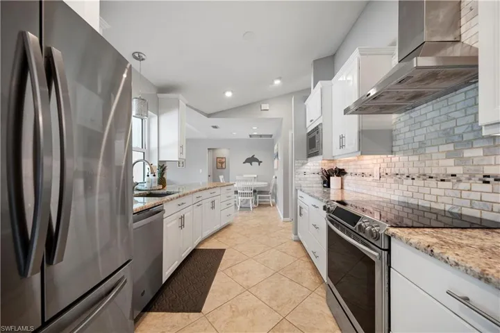 Kitchen featuring white cabinets, stainless steel appliances, hanging light fixtures, and wall chimney range hood