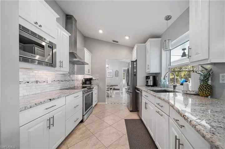 Kitchen with sink, appliances with stainless steel finishes, white cabinetry, light stone countertops, and decorative light fixtures