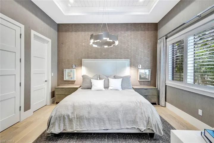 Bedroom with a raised ceiling, a chandelier, and light hardwood / wood-style floors