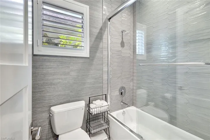 Bathroom with shower / bath combination with glass door, tile walls, and toilet