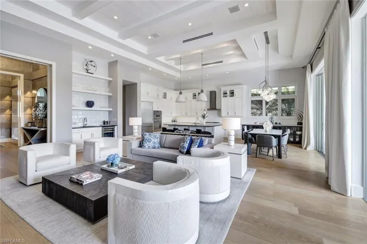 Living room featuring an inviting chandelier, a raised ceiling, wine cooler, light hardwood / wood-style flooring, and beamed ceiling