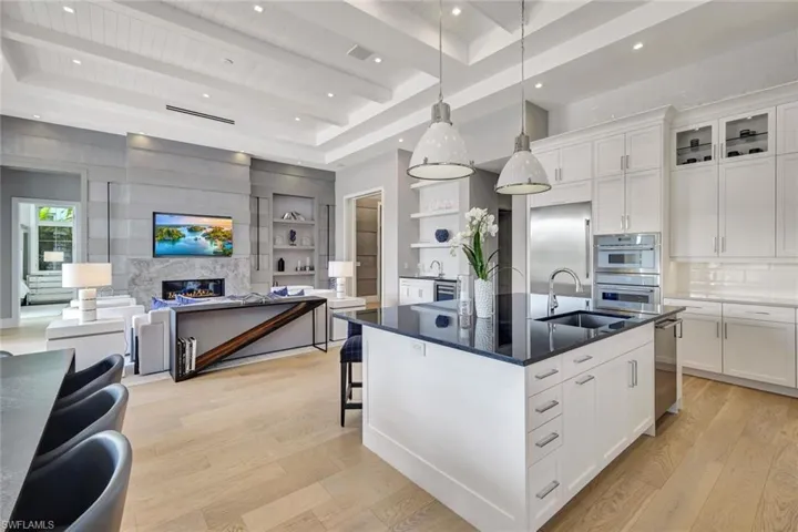 Kitchen featuring sink, decorative light fixtures, a center island with sink, beamed ceiling, and white cabinetry