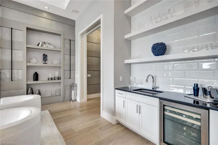 Bar with built in shelves, beverage cooler, sink, light hardwood / wood-style flooring, and white cabinets