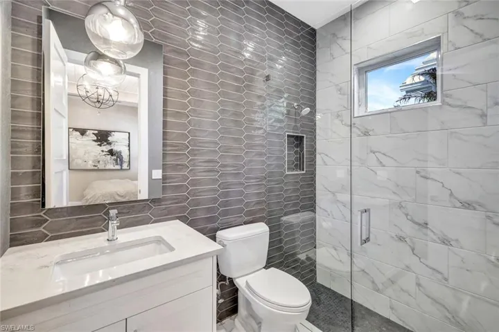 Bathroom featuring toilet, decorative backsplash, a shower with door, vanity, and tile walls