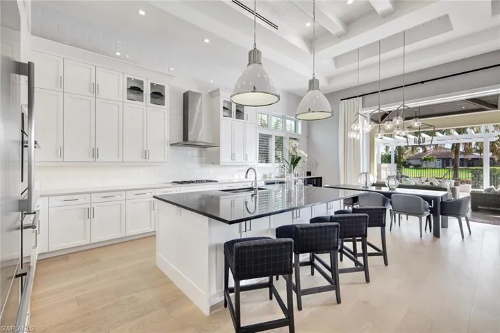 Kitchen featuring white cabinets, light hardwood / wood-style floors, wall chimney range hood, and a kitchen island with sink